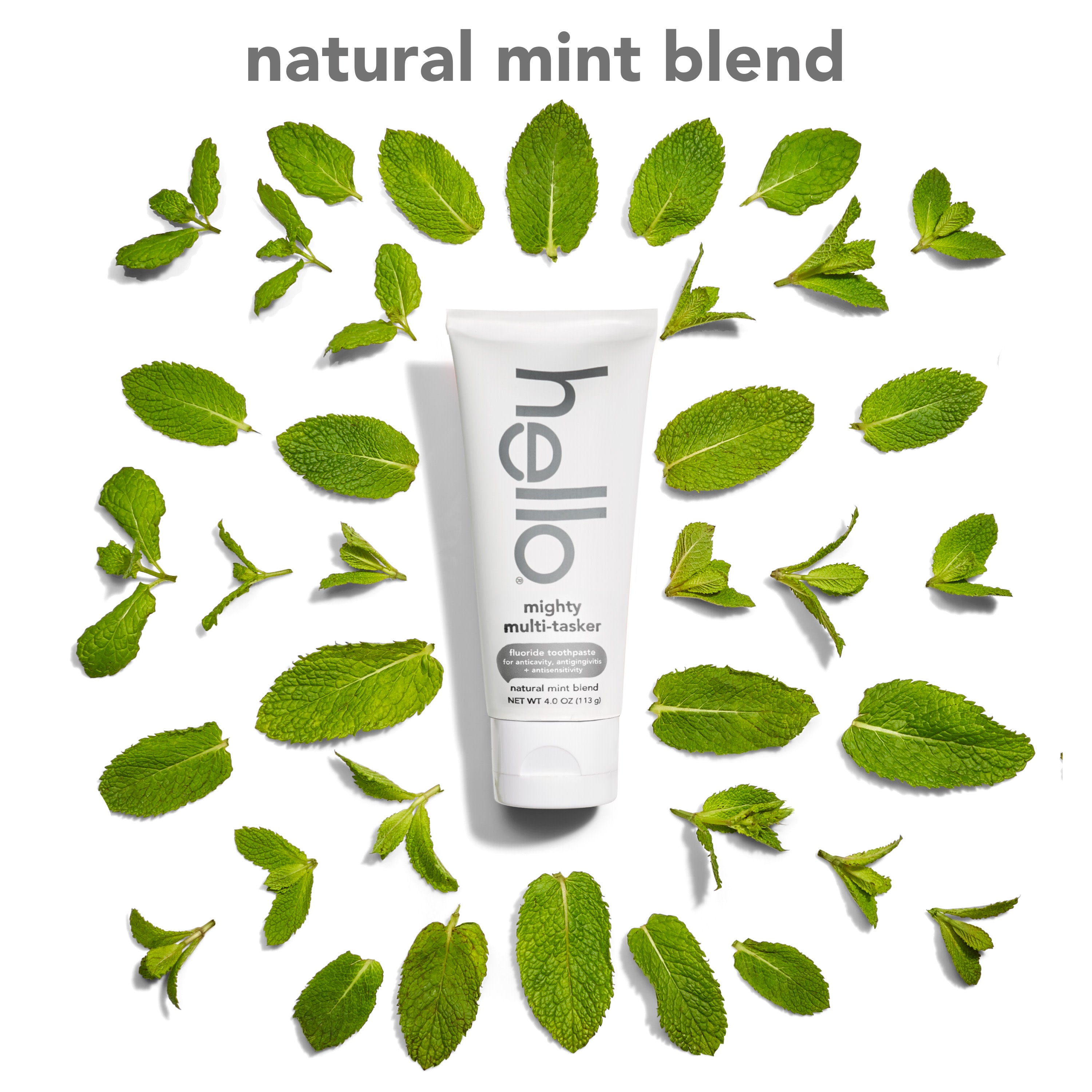 A tube of hello Mighty Multi-Tasker Fluoride Toothpaste against a background of mint leaves. In text: Natural mint blend.