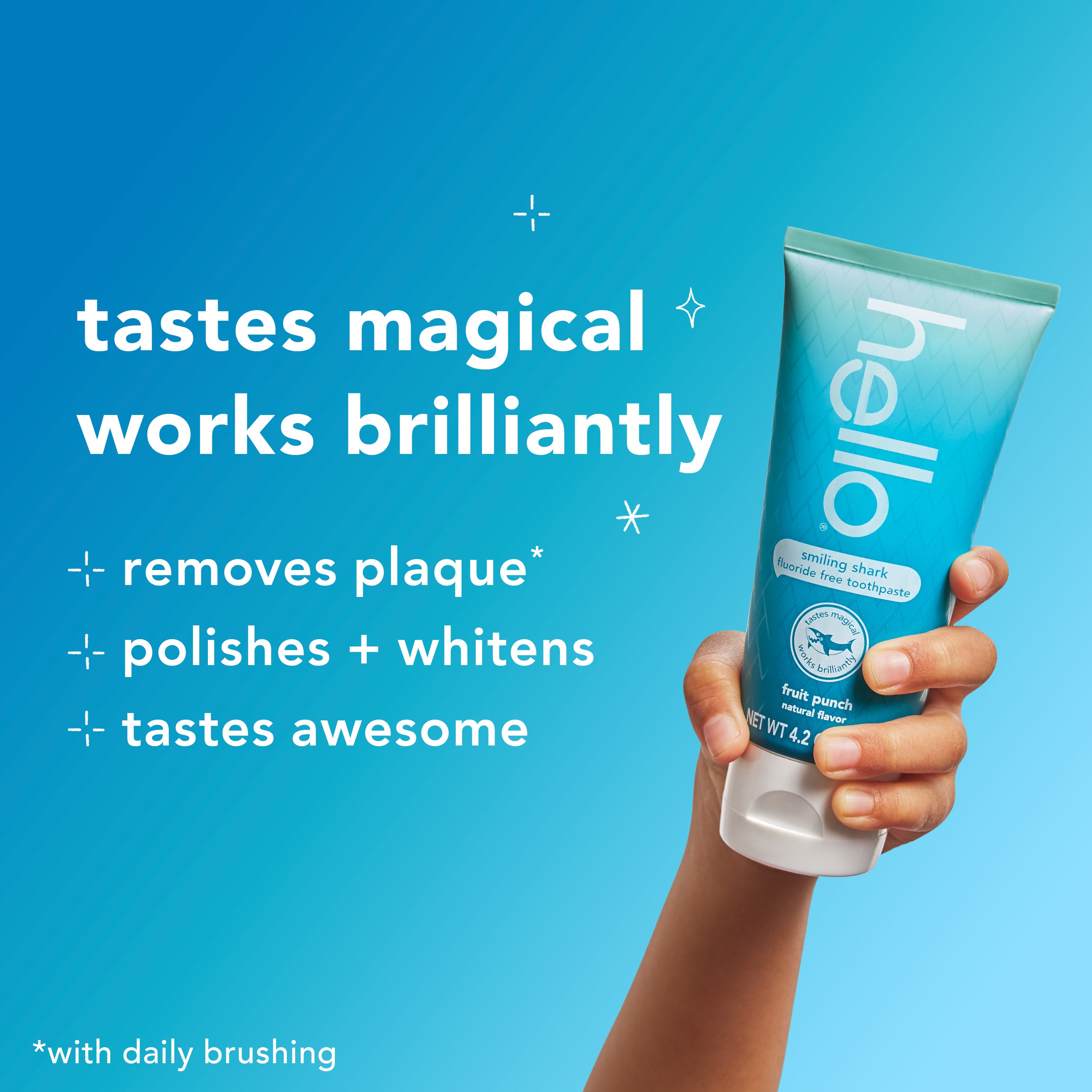 A hand holding up a tube of hello Kids Smiling Shark Fluoride Free Toothpaste. In text: Tastes magical, works brilliantly. Removes plaque*, polishes + whitens, tastes awesome. *With daily brushing.