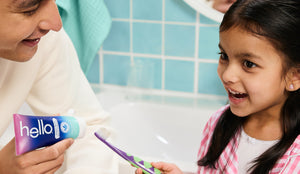 Woman and young girl in a bathroom with a tube of 'hello' toothpaste and a toothbrush.