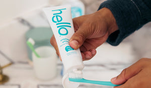 Person holding a tube of 'hello' toothpaste with a blurred bathroom background