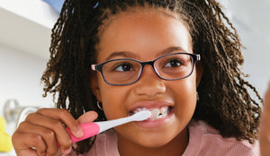 Young girl with glasses brushing her teeth in a bathroom setting