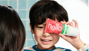 Child holding a tube of toothpaste with 'hello' branding in front of a mirror.
